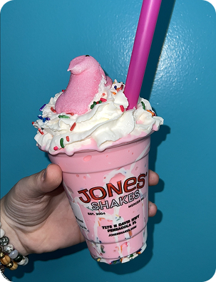 Hand holding a strawberry milkshake with whipped cream in a Jones Shakes cup